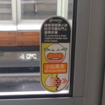 A warning sign in Taipei's metro with a dramatic crying emoji saying to keep your hands clear of closing doors or you'll get hurt.